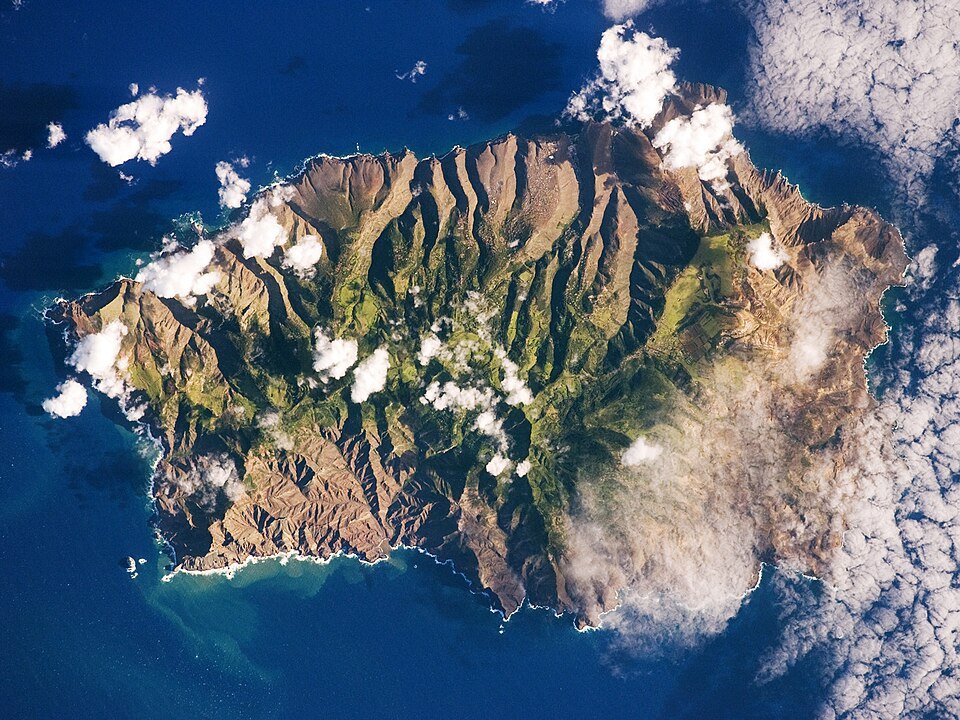 St. Helena island with steep ridges, ravines and scattered clouds, seen from orbit.