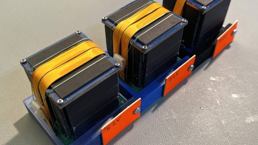 Three ERMINAZ-2 PocketQube satellites with solar panels and folded tape antennas in a transport fixture